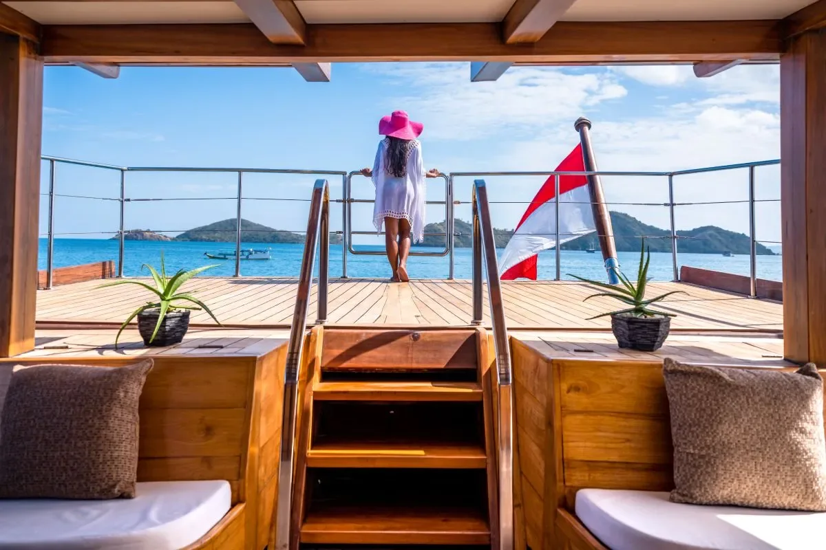 A woman in a sunhat looking out from the stern deck of the Lamima phinisi at islands on the horizon