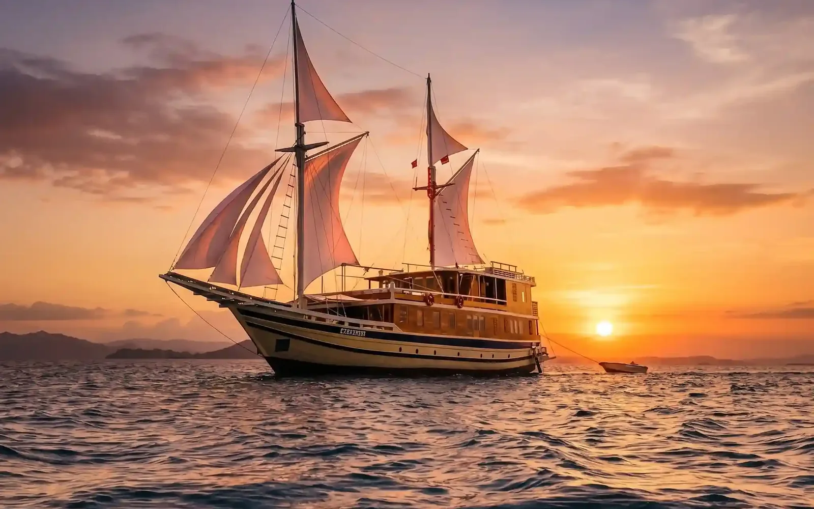 The Catnasze phinisi under full sail at sunset, with a tender boat trailing behind