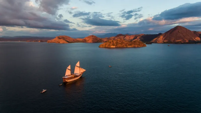 A wooden phinisi under sail at sunset among the Komodo islands