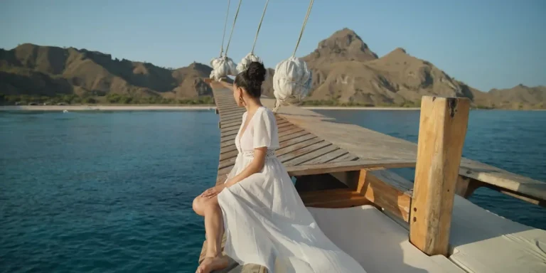 Woman in white dress on a phinisi bowsprit in Komodo