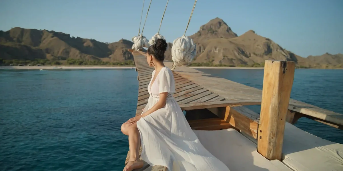 Woman in white dress on a phinisi bowsprit in Komodo